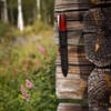 knife in sheath hanging against log cabin outside wall