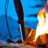 Red with fire striker in handle, blade stuck in wood next to fire
